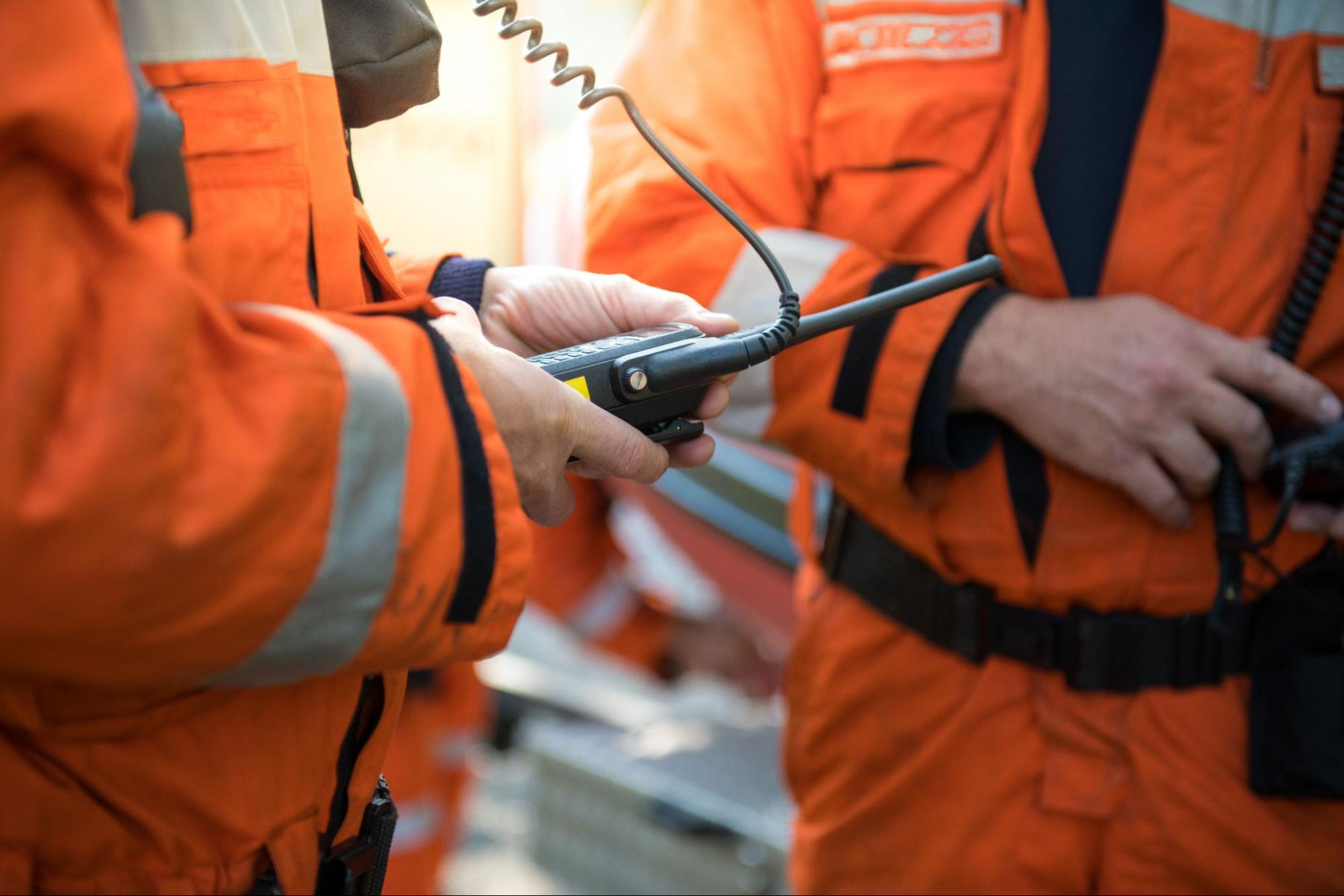 two people in orange jumpsuits standing and talking on walky-talky