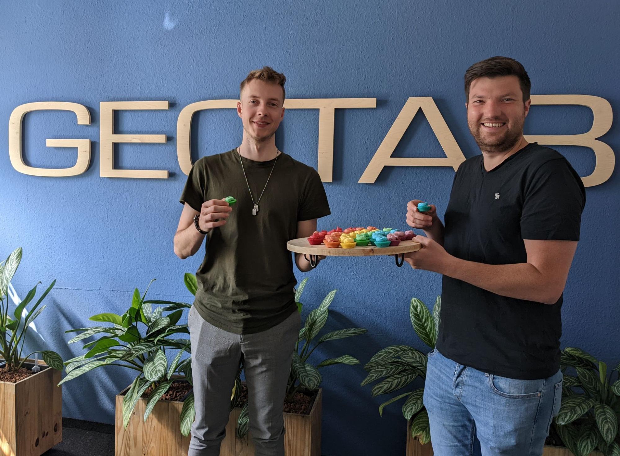 Two Geotabbers celebrating Pride in the office with rainbow-colored cupcakes.