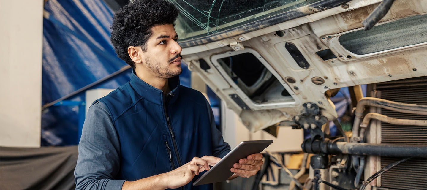 A man outside of a fleet vehicle looking at a tablet