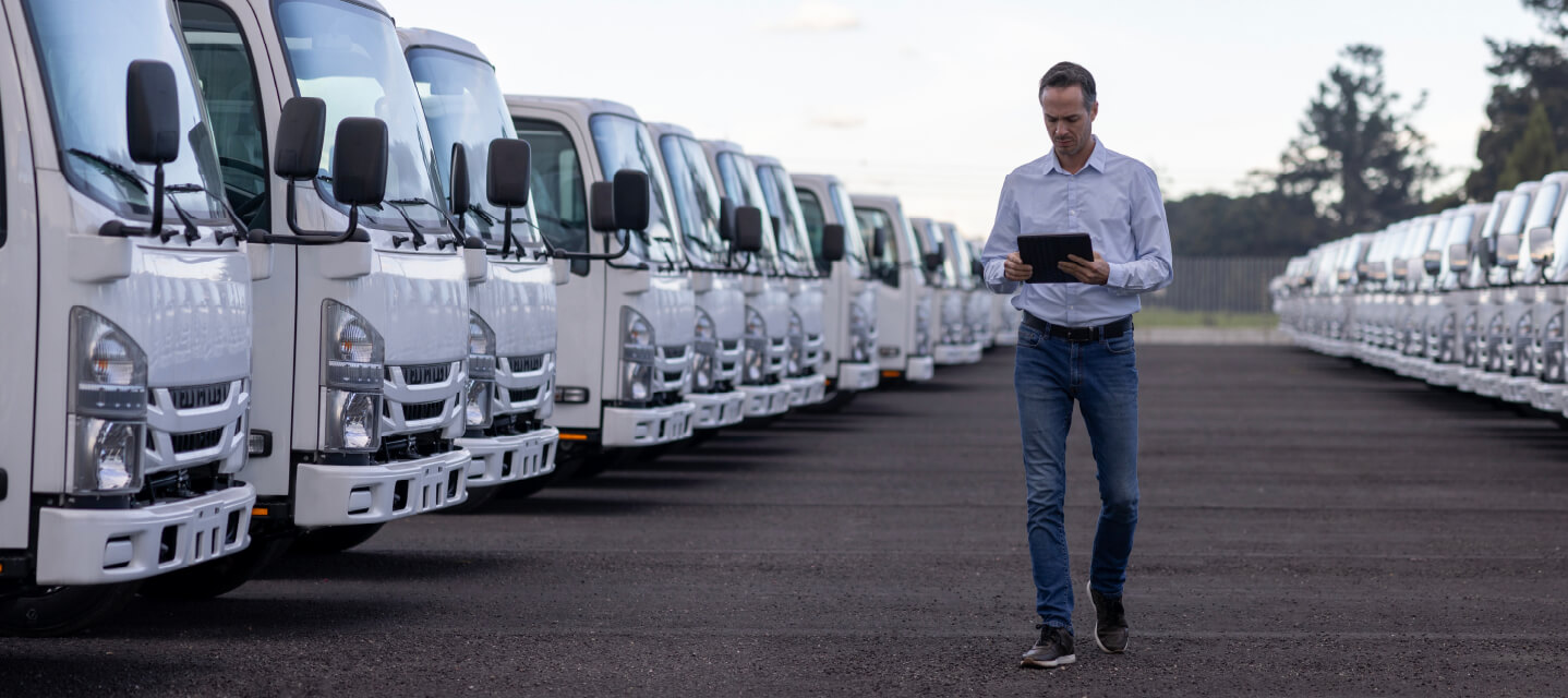 a man looking at a tablet and walking through a line of fleet vehicles. 