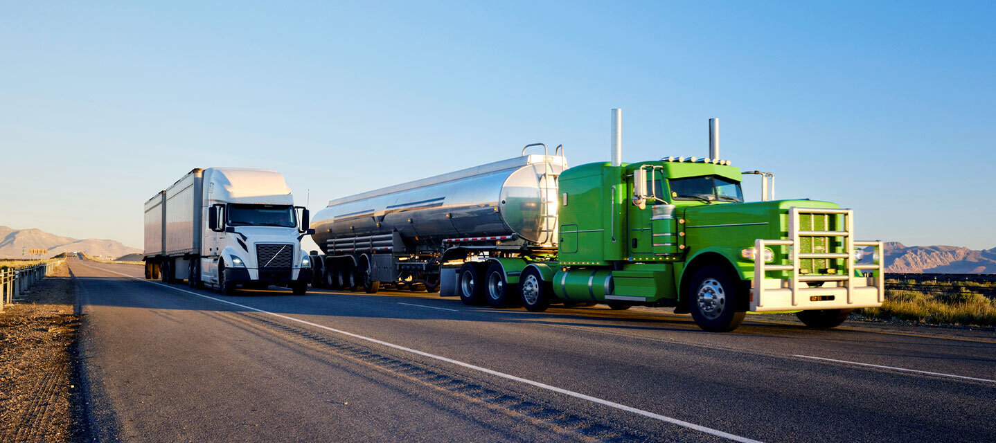 one white fleet truck and one green gas fleet truck driving down the highway