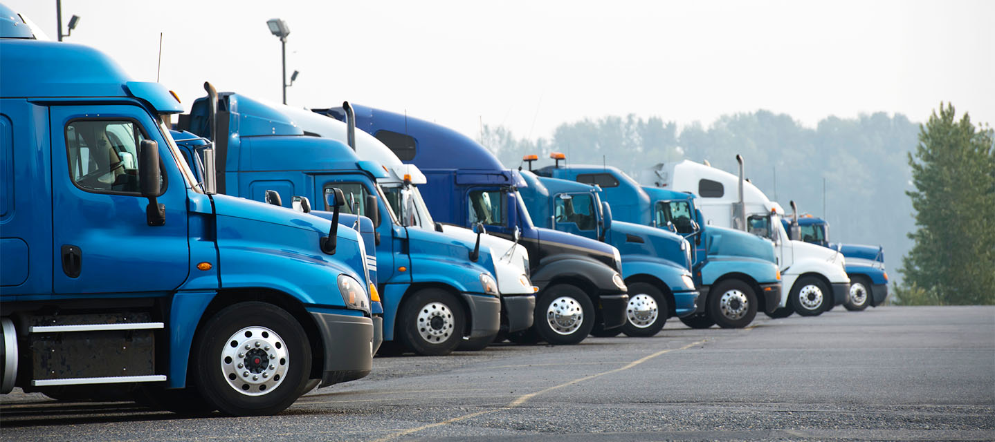 A line up of blue and white commercial semi trucks at a truck stop parking lot.