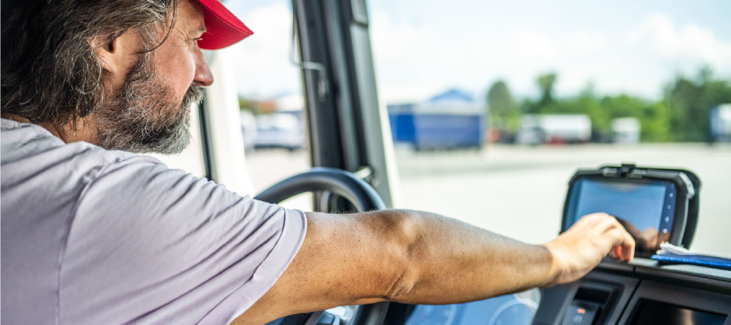 A man sitting in the driver’s seat of a vehicle, touching a GPS screen. 
