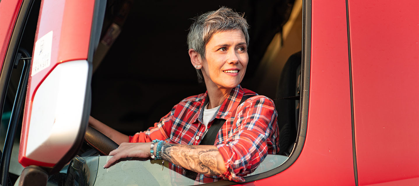 A person in the driver's seat of a red truck wearing a plaid shirt looking out the window.