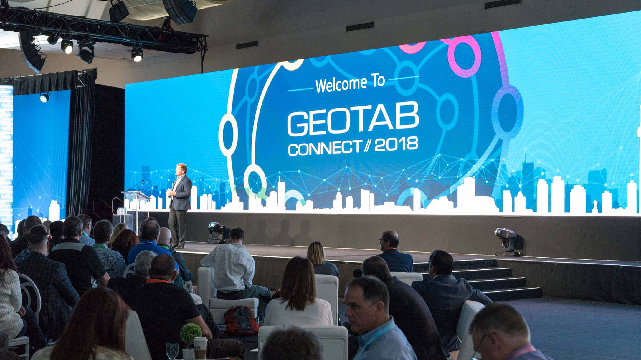 A room full of people sitting and watching someone present at a conference