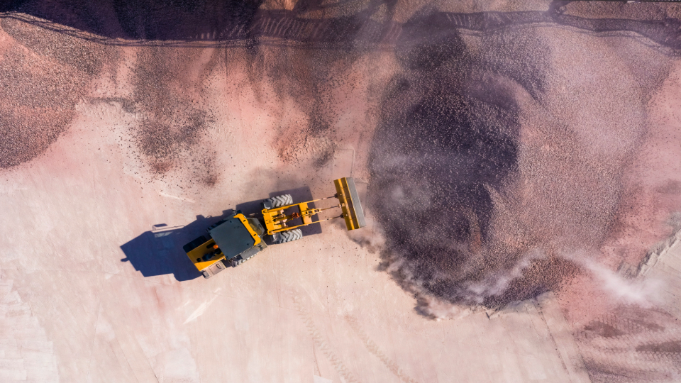 An aerial view shows a yellow bulldozer moving dirt, creating dust.