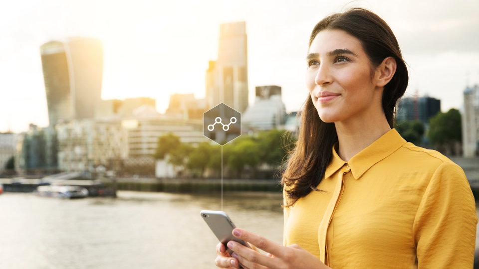 Mujer sonriente con un celular y ciudad de fondo, simbolizando eficiencia y tecnología para optimizar el mantenimiento de flota.