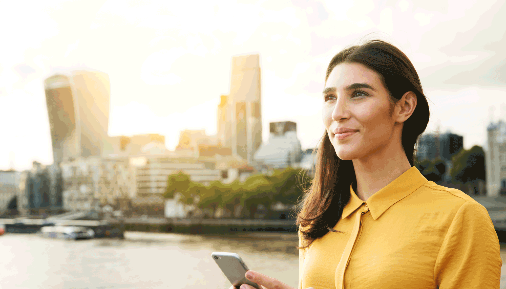 Mujer sonriente con un celular y ciudad de fondo, simbolizando eficiencia y tecnología para optimizar el mantenimiento de flota.