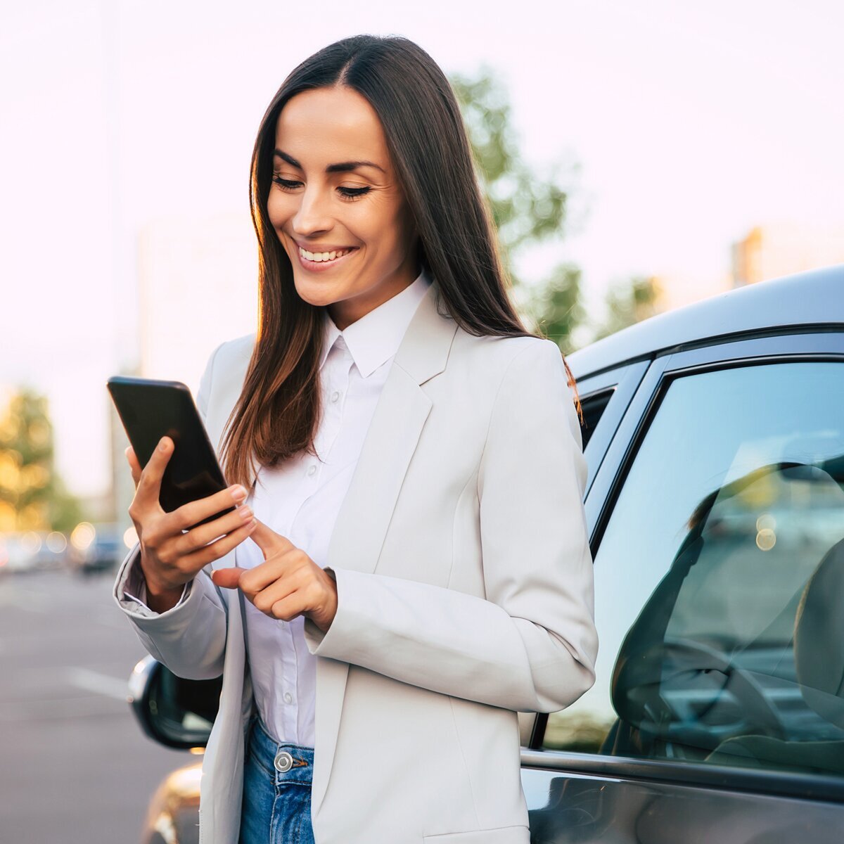 Smiling woman using smartphone by car.