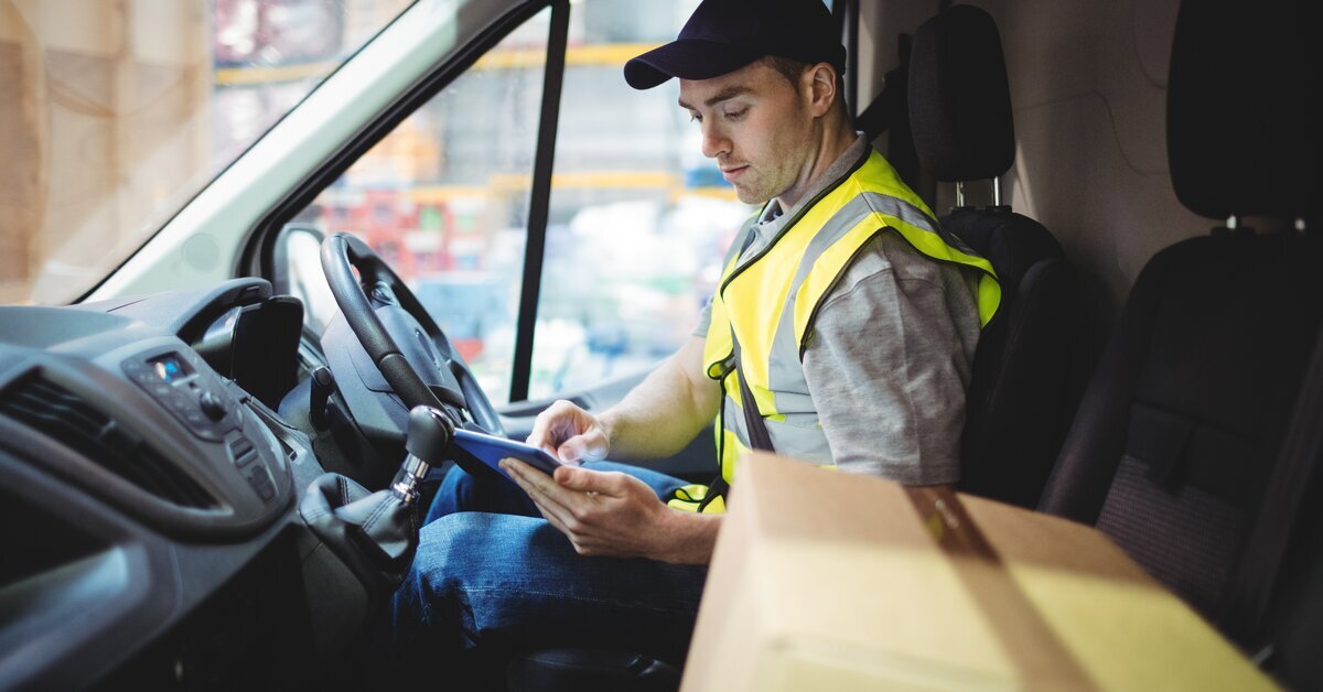 Delivery driver in a high‑visibility vest using a tablet inside a van.