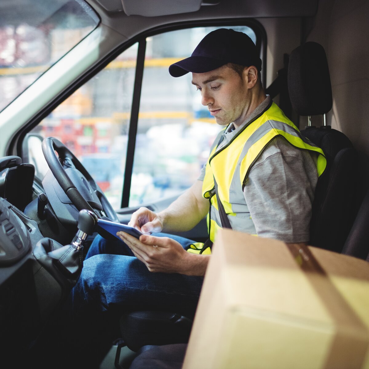 Delivery driver in a high‑visibility vest using a tablet inside a van.