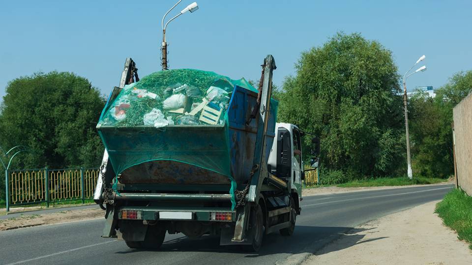Camion della spazzatura di colore verde in circolazione in una strada soleggiata
