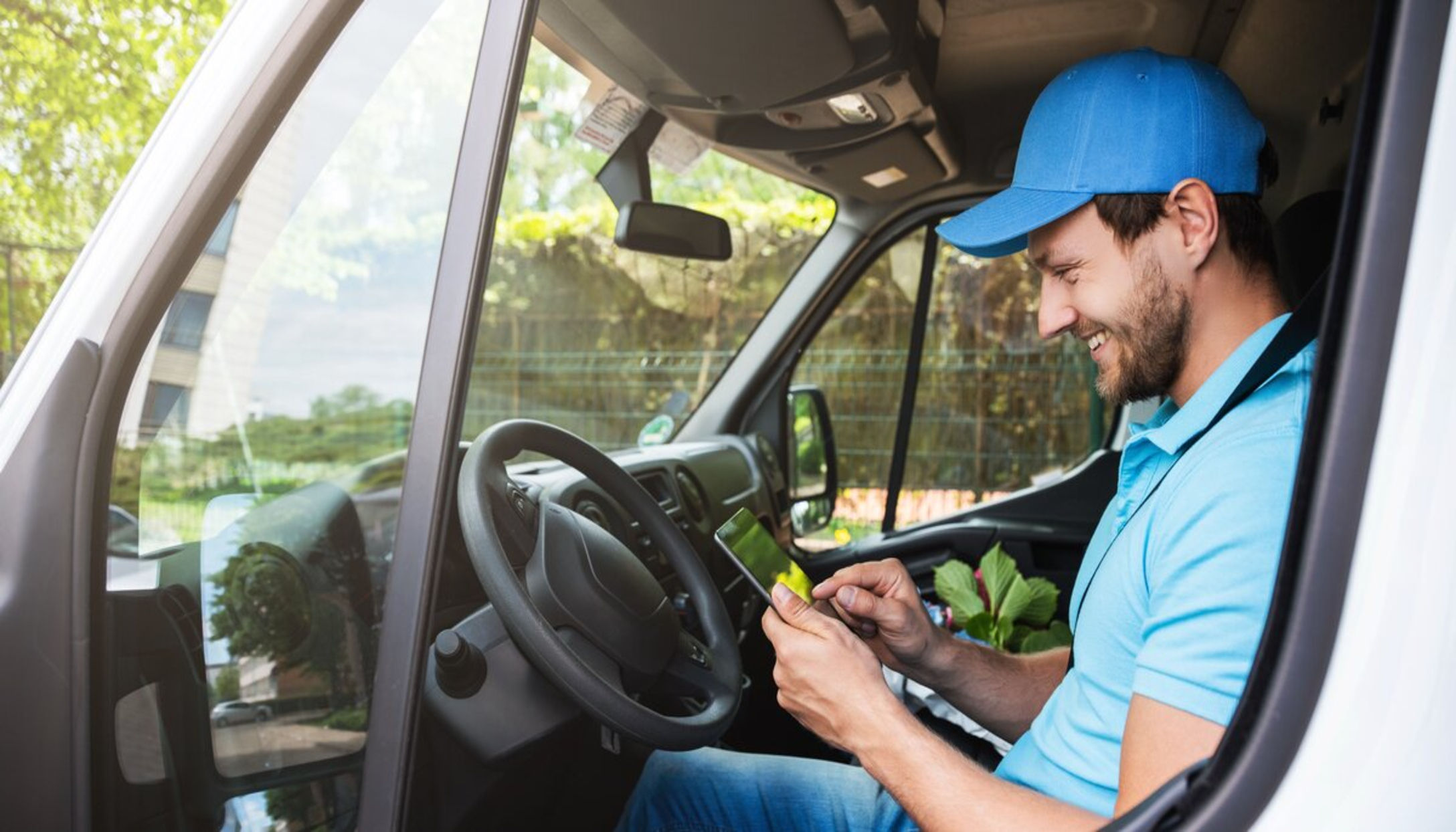Een tevreden koerier in zijn bestelbus controleert informatie op een mobiel apparaat dat hij in zijn handen houdt.