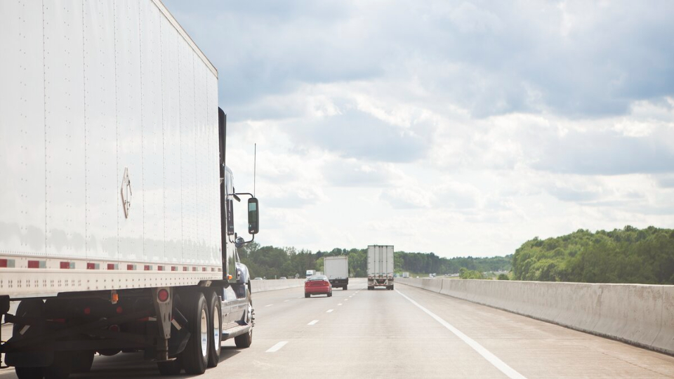Een vrachtwagen rijdt over een snelweg met een blauwe hemel en wolken op de achtergrond.