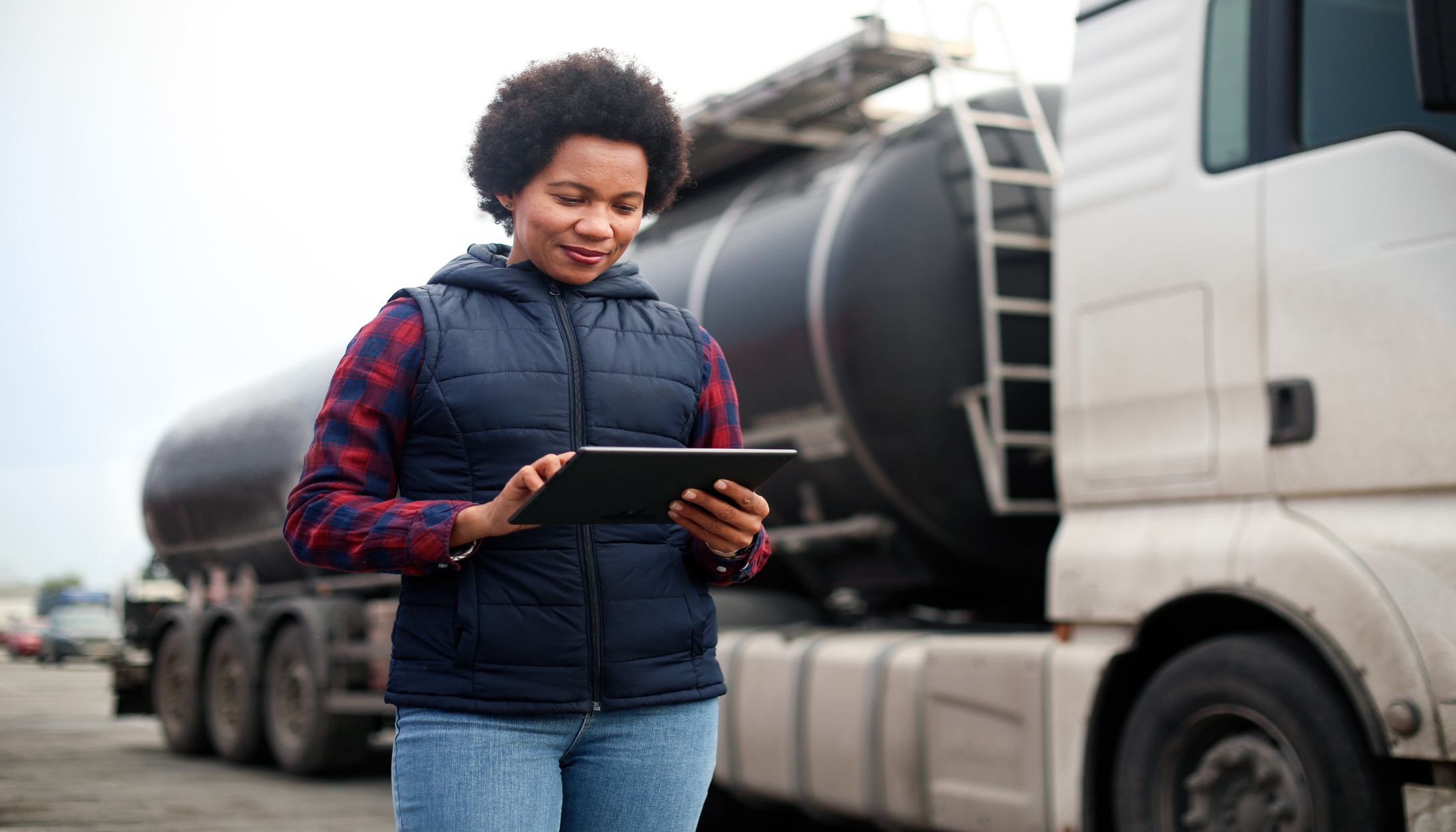 Vrouwelijke vrachtwagenchauffeur of fleetmanager kijkt op een tablet bij haar vrachtwagen.