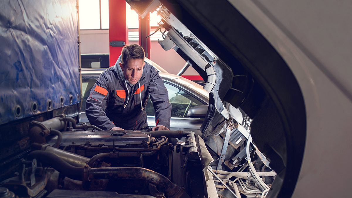 Mecânico inspecionando o motor de um veículo em uma oficina, representando a importância da manutenção de frota e da prevenção de falhas.