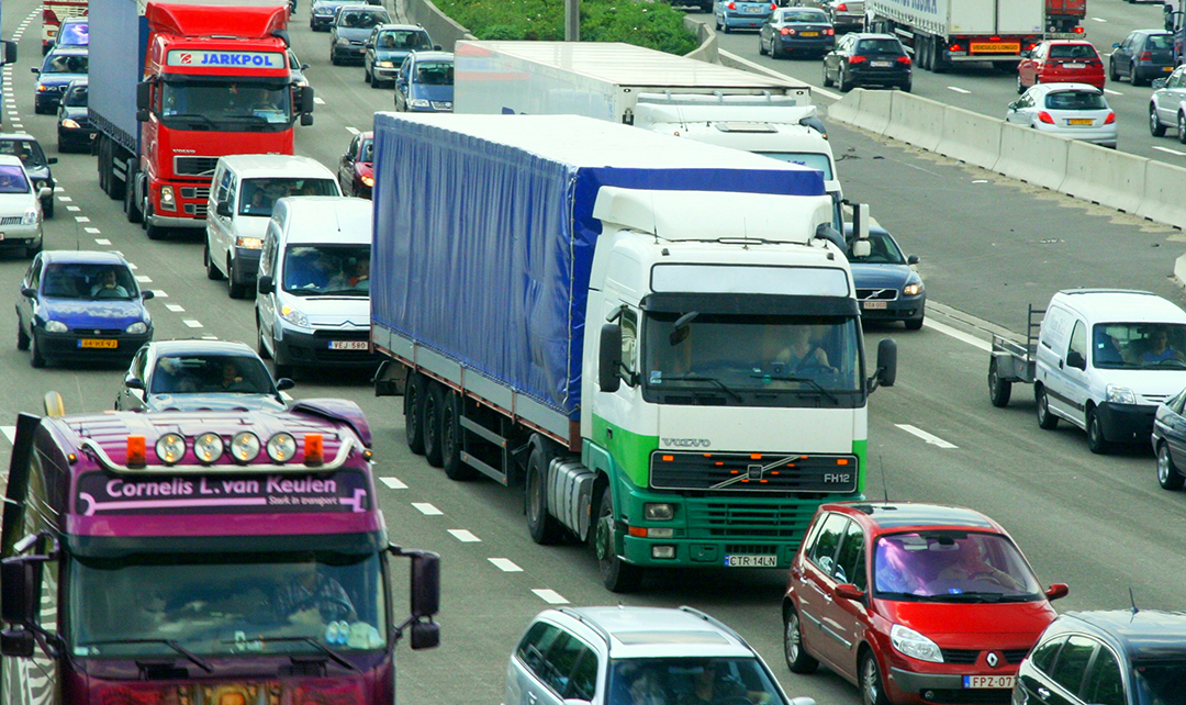 Imagem de trânsito com caminhões e carros, ilustrando a logística em período de alta demanda e a otimização do last mile.