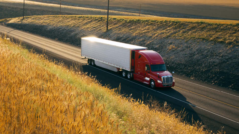 Class 8 truck driving down highway with green pastures surrounding it