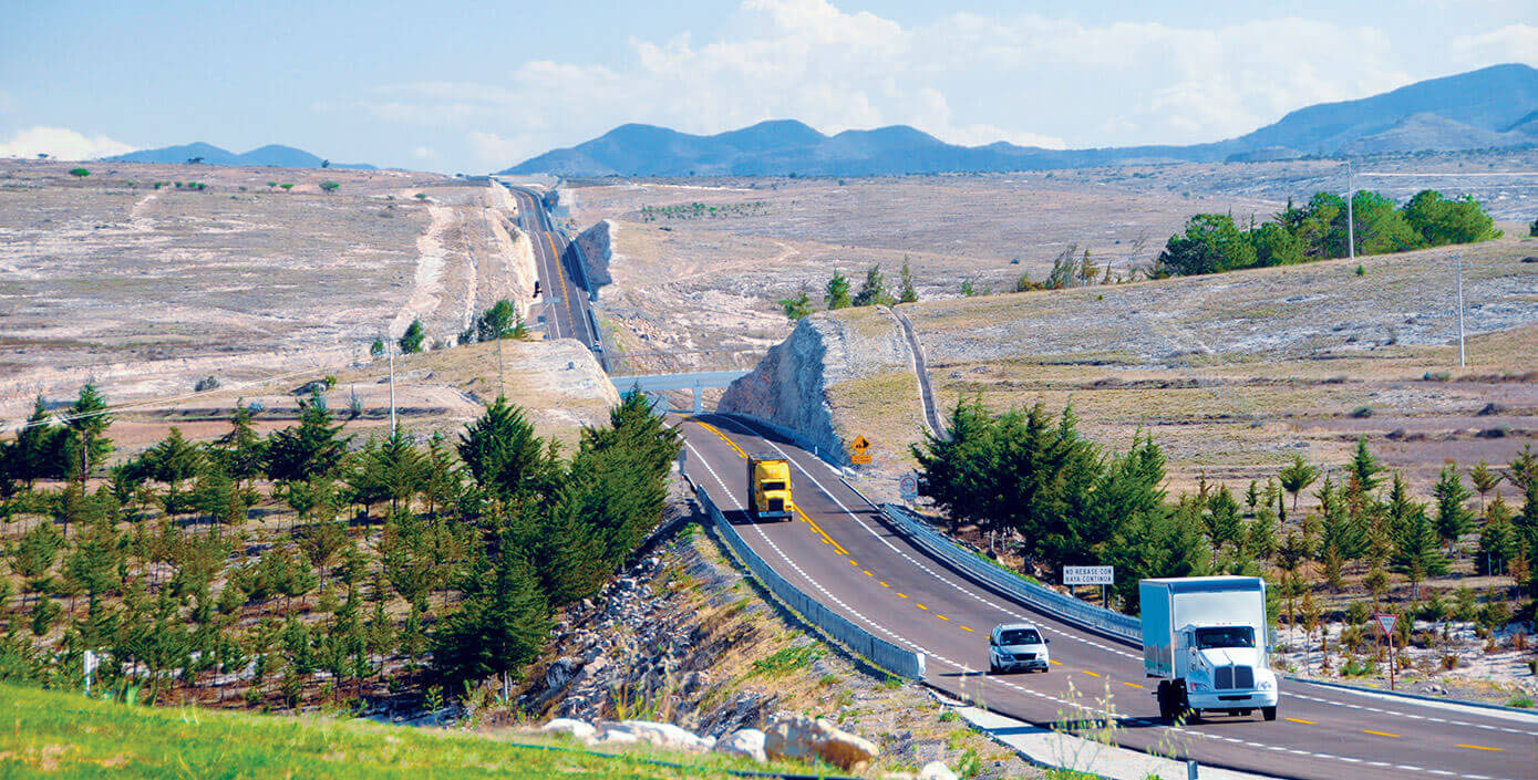Transportation trucks and car following each other down open road.