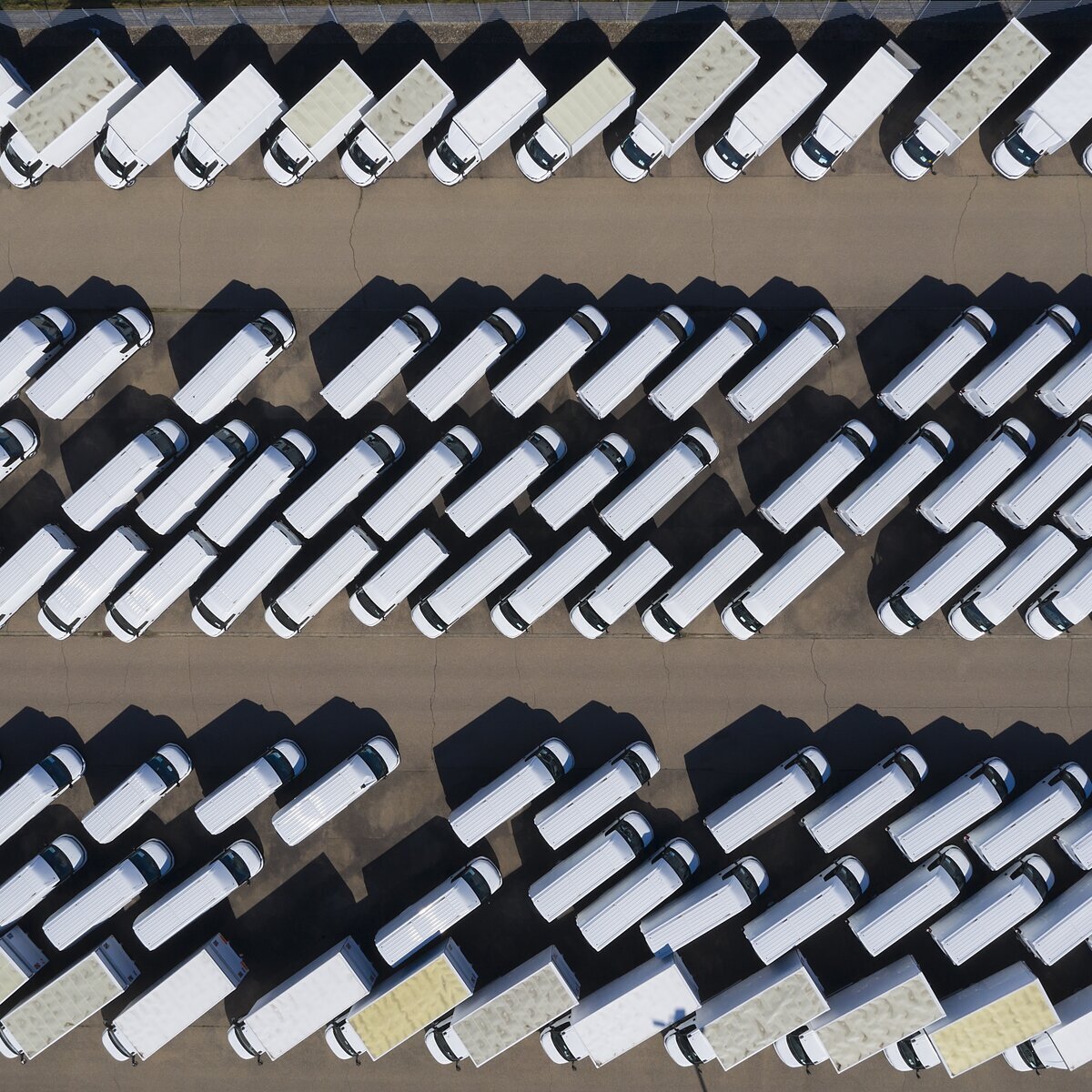 Aerial view of a large fleet of white delivery vans and trucks parked in rows.