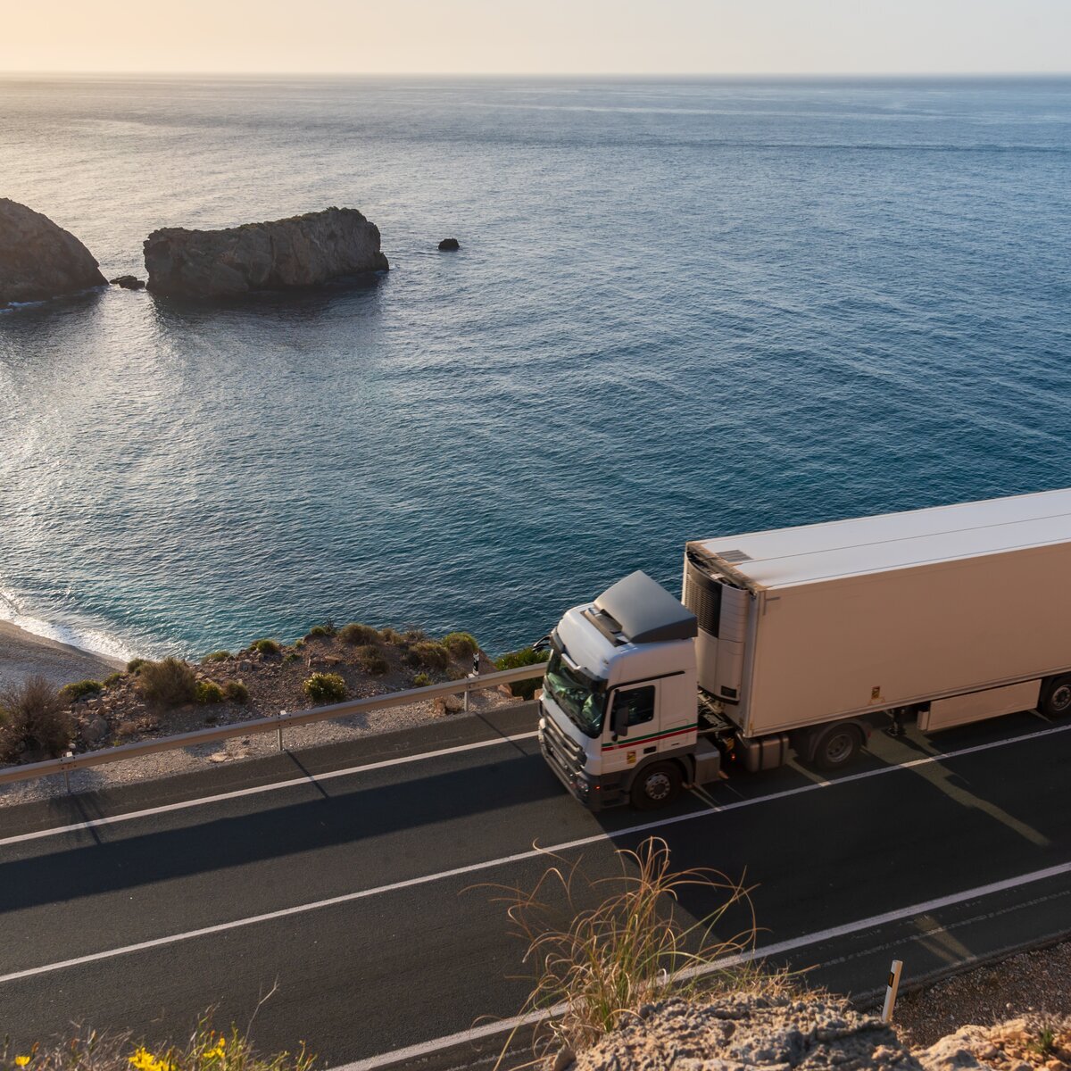 Refrigerated lorry driving along a coastal highway.