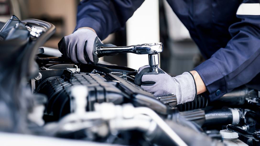 A mechanic in gloves is tightening a bolt on a vehicle engine in a workshop